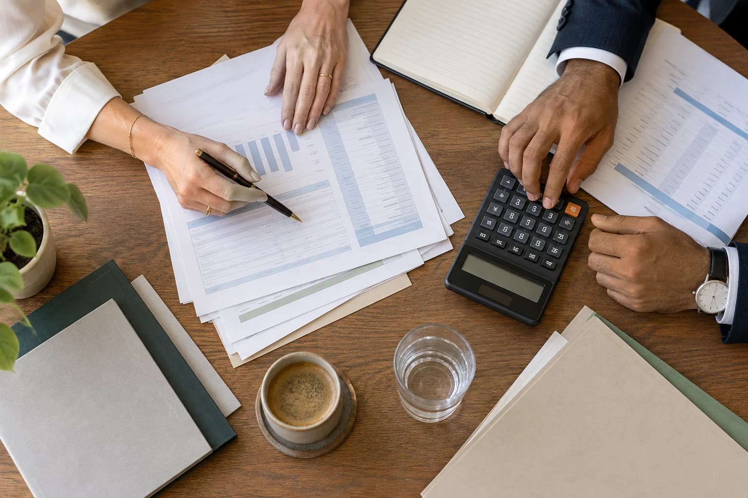 An overhead view of two professionals planning costs with a calculator, papers and folders.
