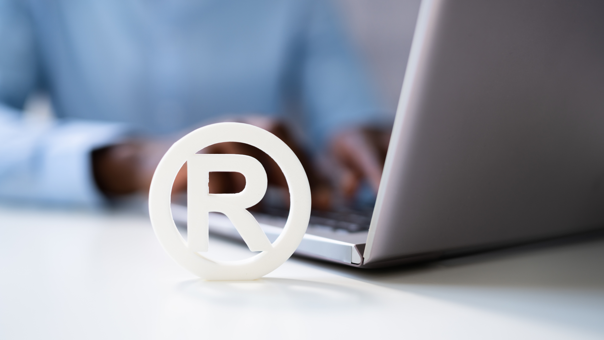 Person using laptop and registered trademark logo in foreground