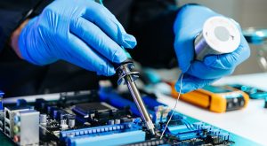 A pair of hands wearing blue gloves, working on electrical components for a mobile device.
