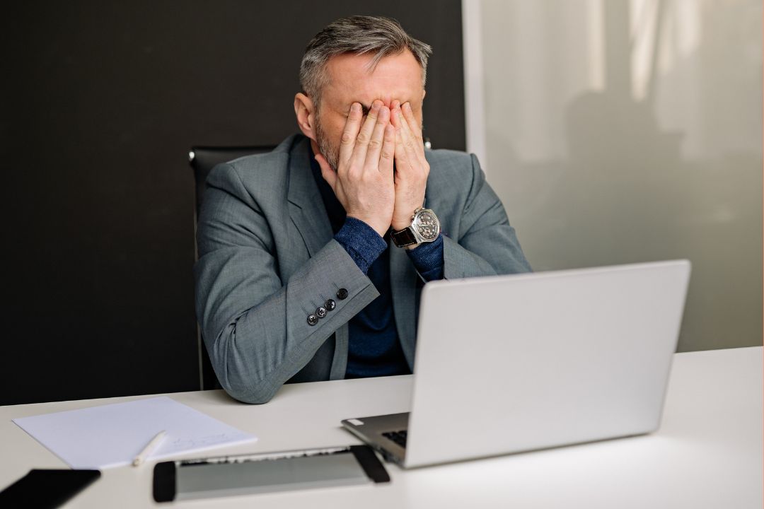 A man sat at a laptop with his head in his hands as he realises someone has trademarked his business name