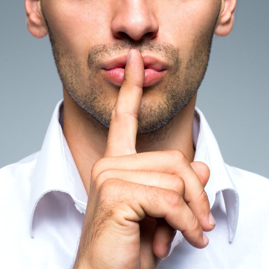 A man with his finger infront of his lips, withholding a secret