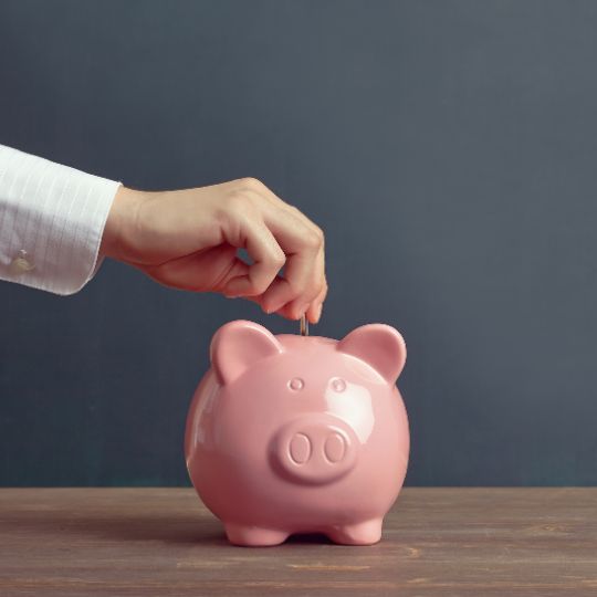 A hand dropping coins into a pink piggy bank
